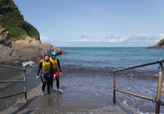 Coasteering participants walking out of the sea onto slipway wearing helmets and buoyancy aids