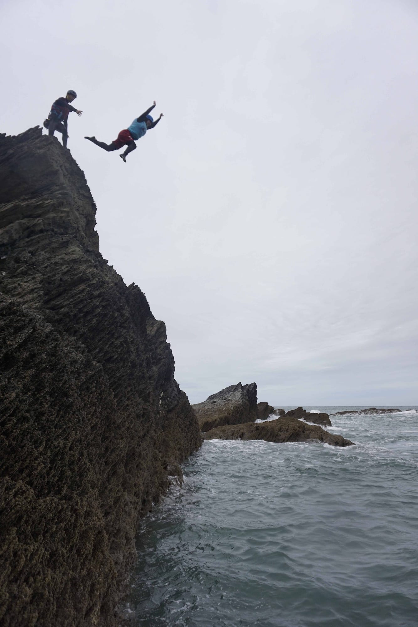 Coasteering participant jumping from rocky cliff into the sea